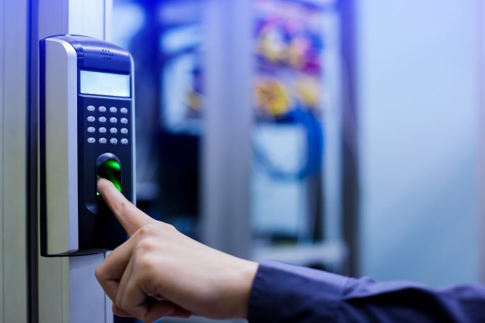 Hand pressing a finger on a wall-mounted fingerprint scanner with keypad and display