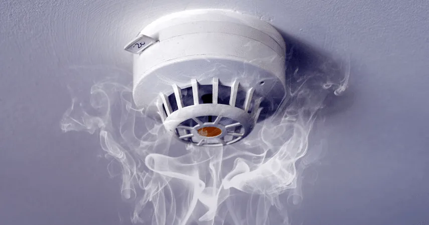 White ceiling smoke detector with wisps of smoke rising around it